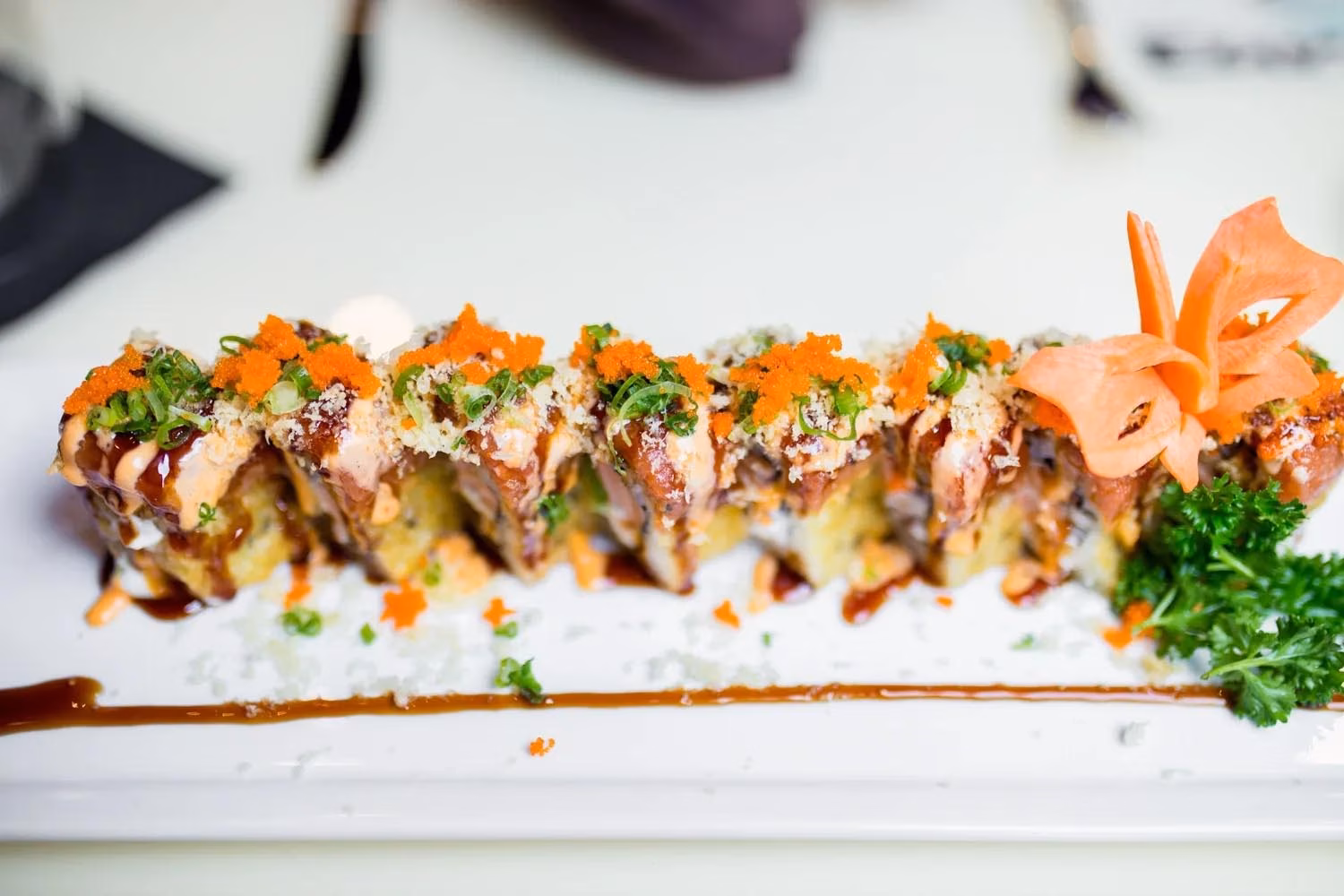 A plate of sushi rolls topped with orange roe and green onions.