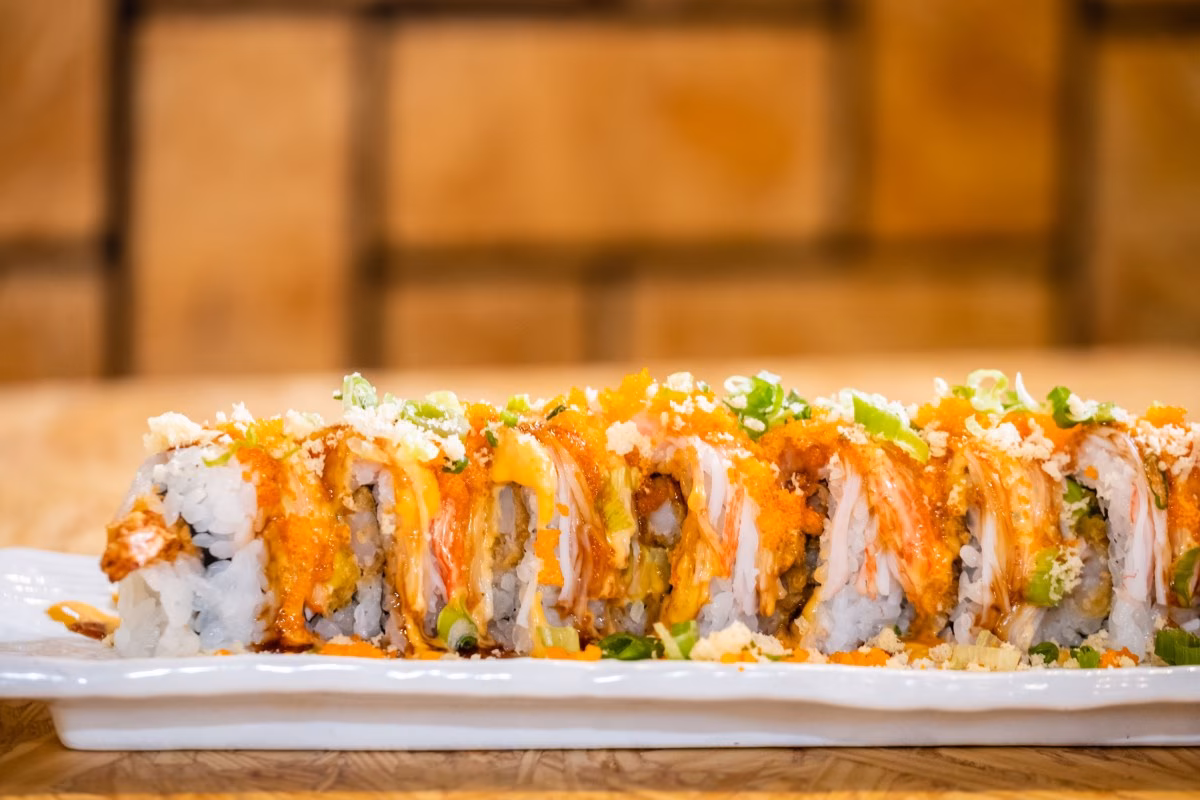 Sushi rolls topped with orange sauce, roe, white flakes, and green onions.
