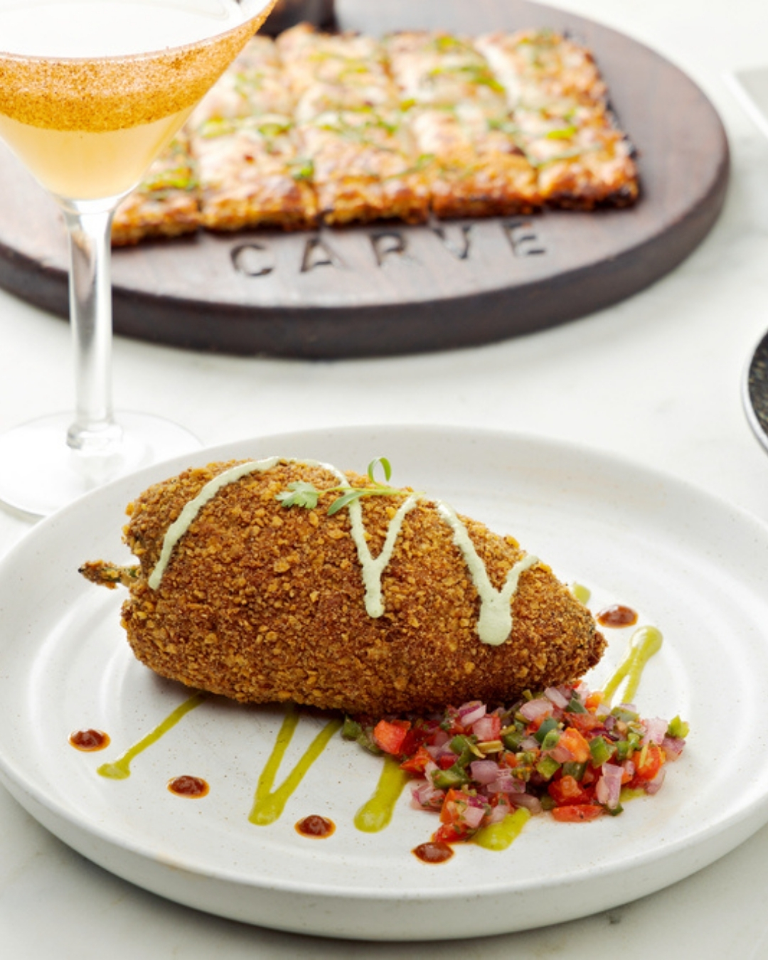 Golden-brown breaded chili with salsa, cocktail glass, and flatbread.