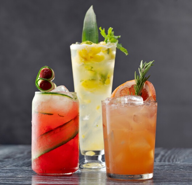 Three colorful cocktails with various fruit and herb garnishes.