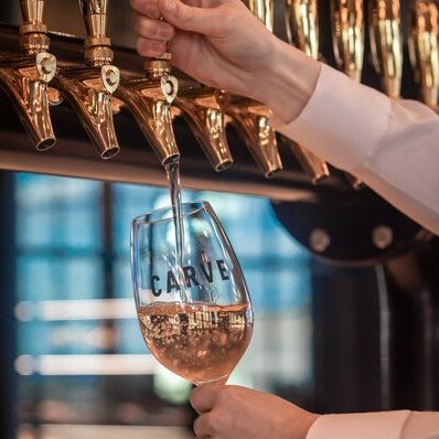 Beverage pouring from golden tap into a branded wine glass.