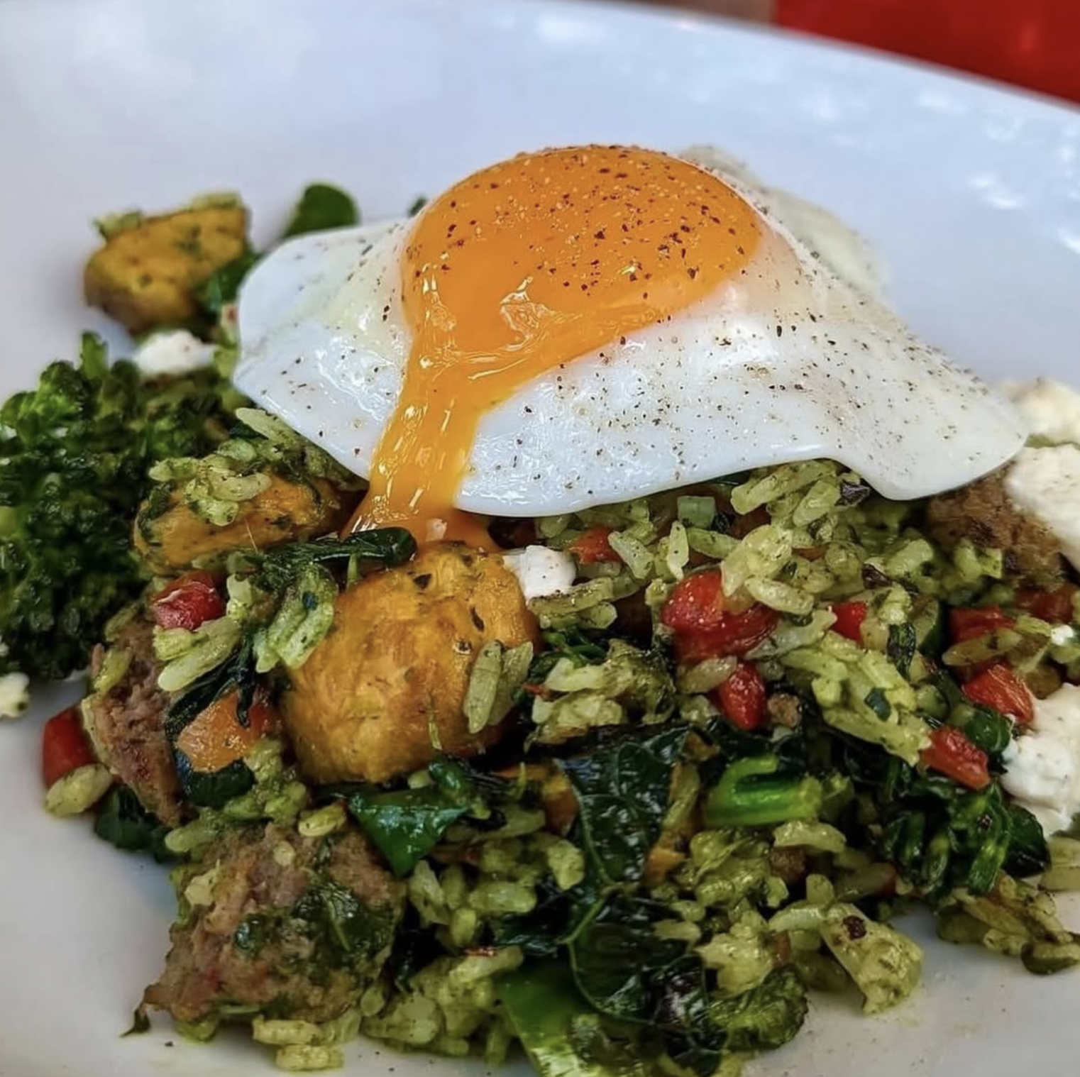 Close-up of a fried egg over green rice, vegetables, and meat.