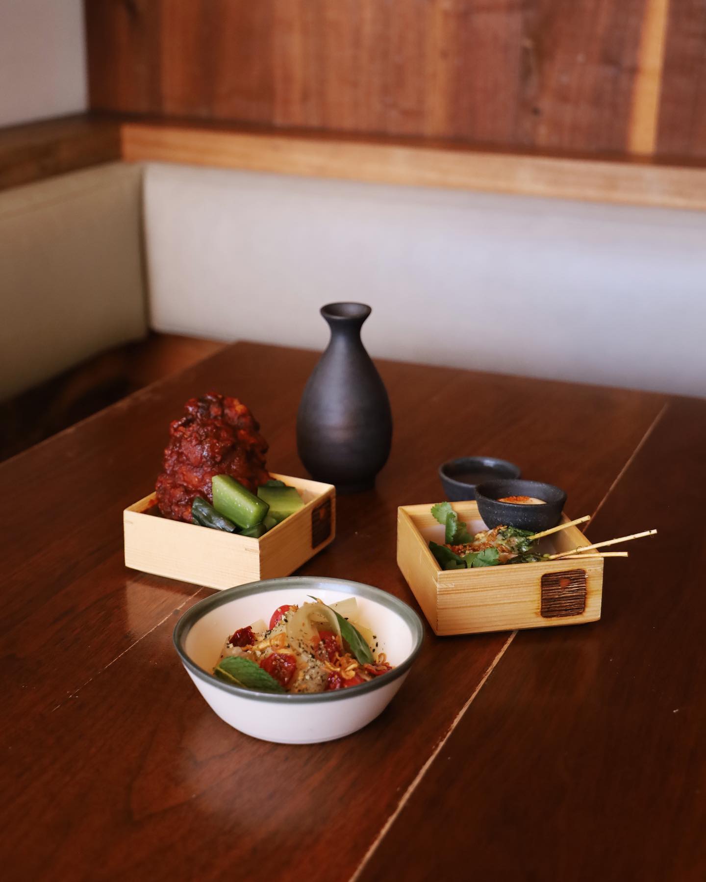 Three small food dishes and a black vase on a wooden table.