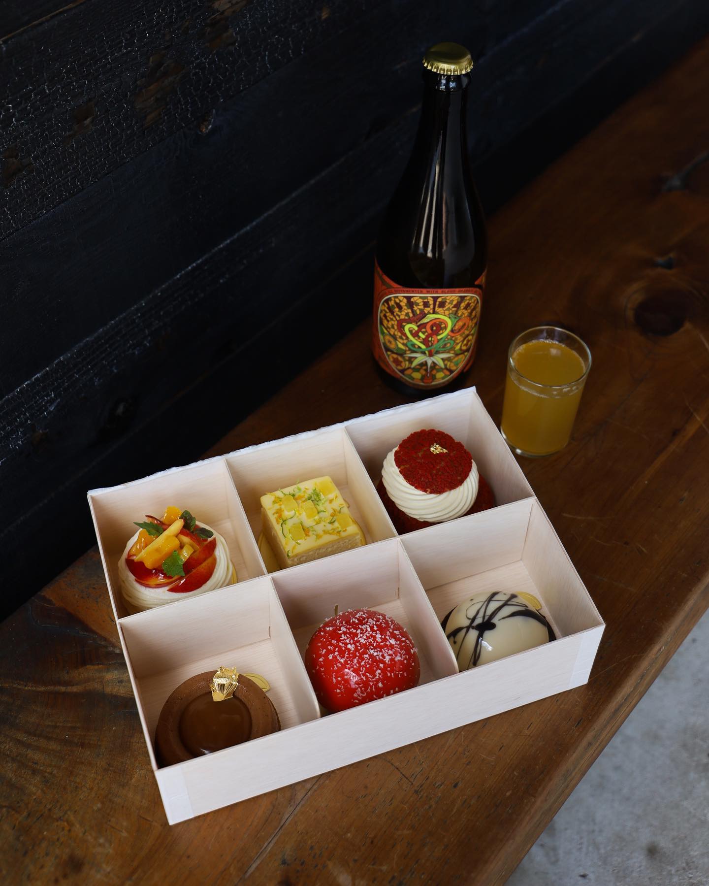 Six assorted pastries in a box, a bottle, and a drink.