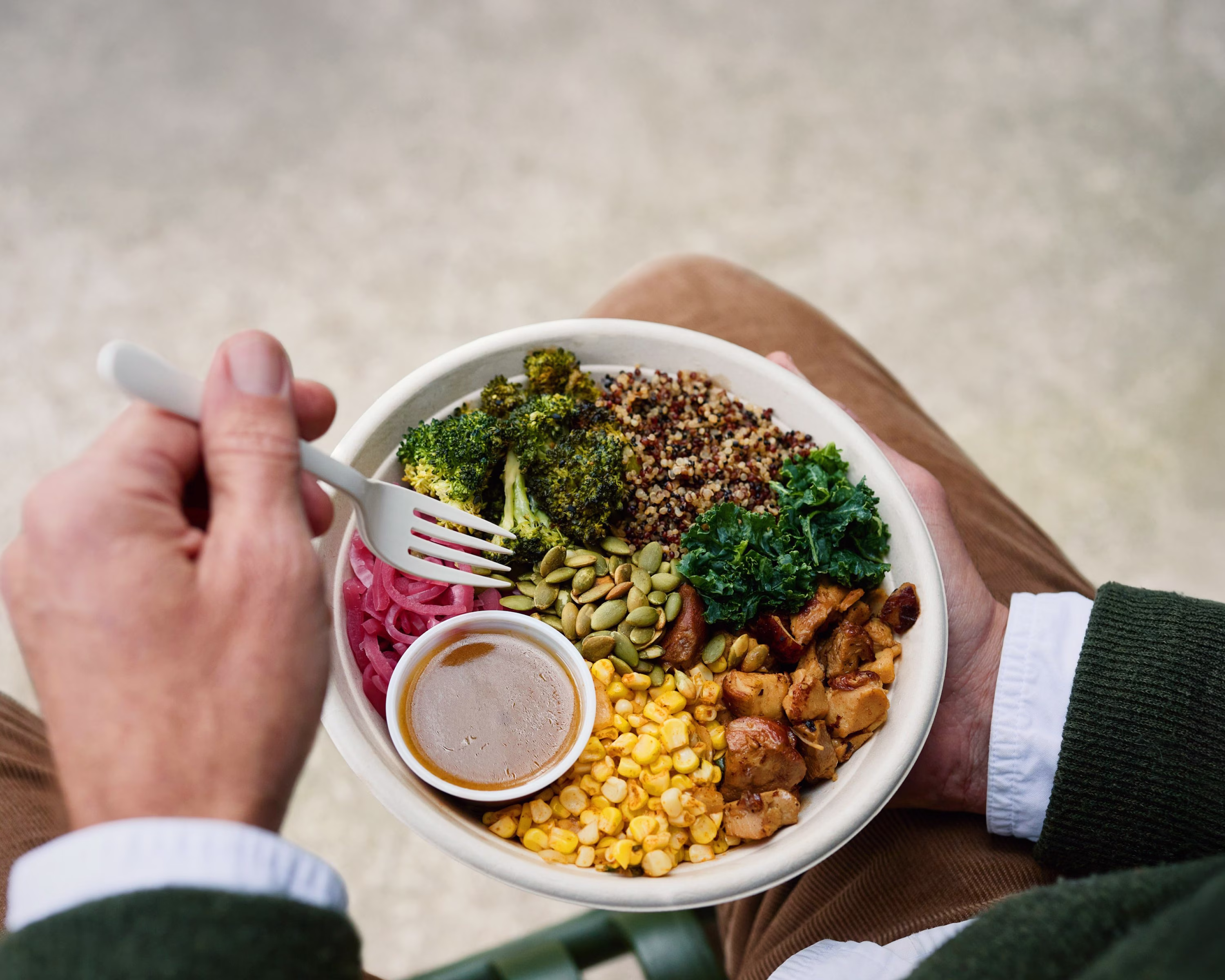 Person holding a colorful meal bowl with fork over their lap.
