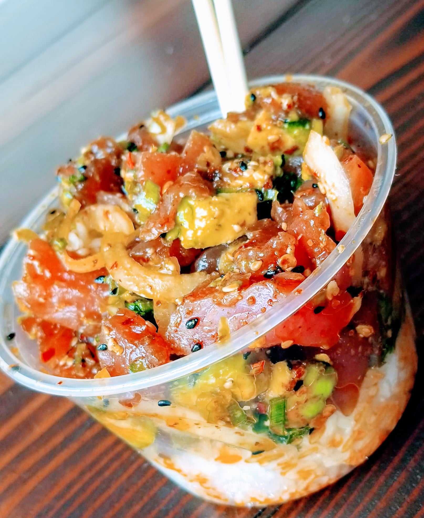 Poke bowl in clear cup with tuna, avocado, onions, and chopsticks.