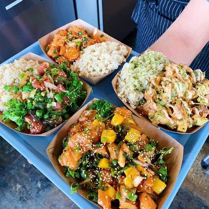 Four bowls of various poke with rice on a blue tray.