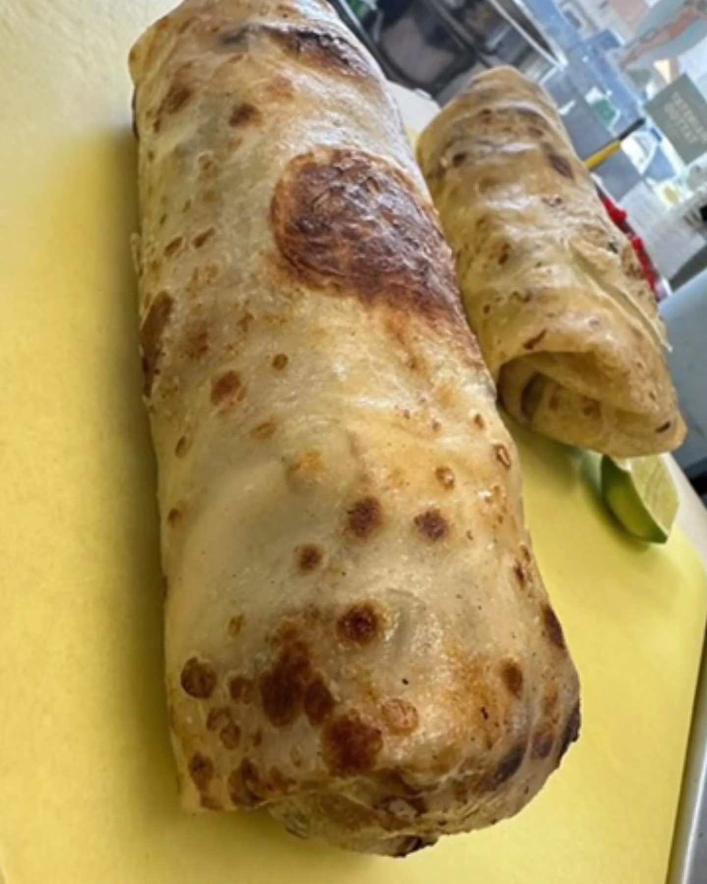 Two large, golden-brown burritos on a yellow surface, with lime.