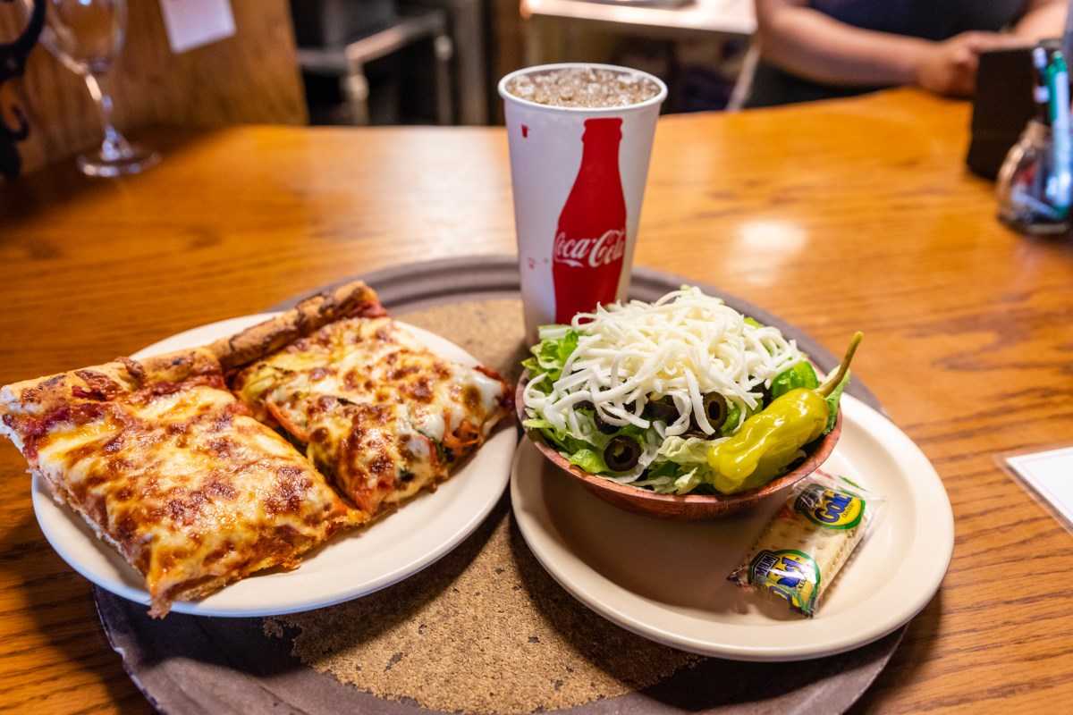 Two pizza slices, a side salad, and Coca-Cola on a table.