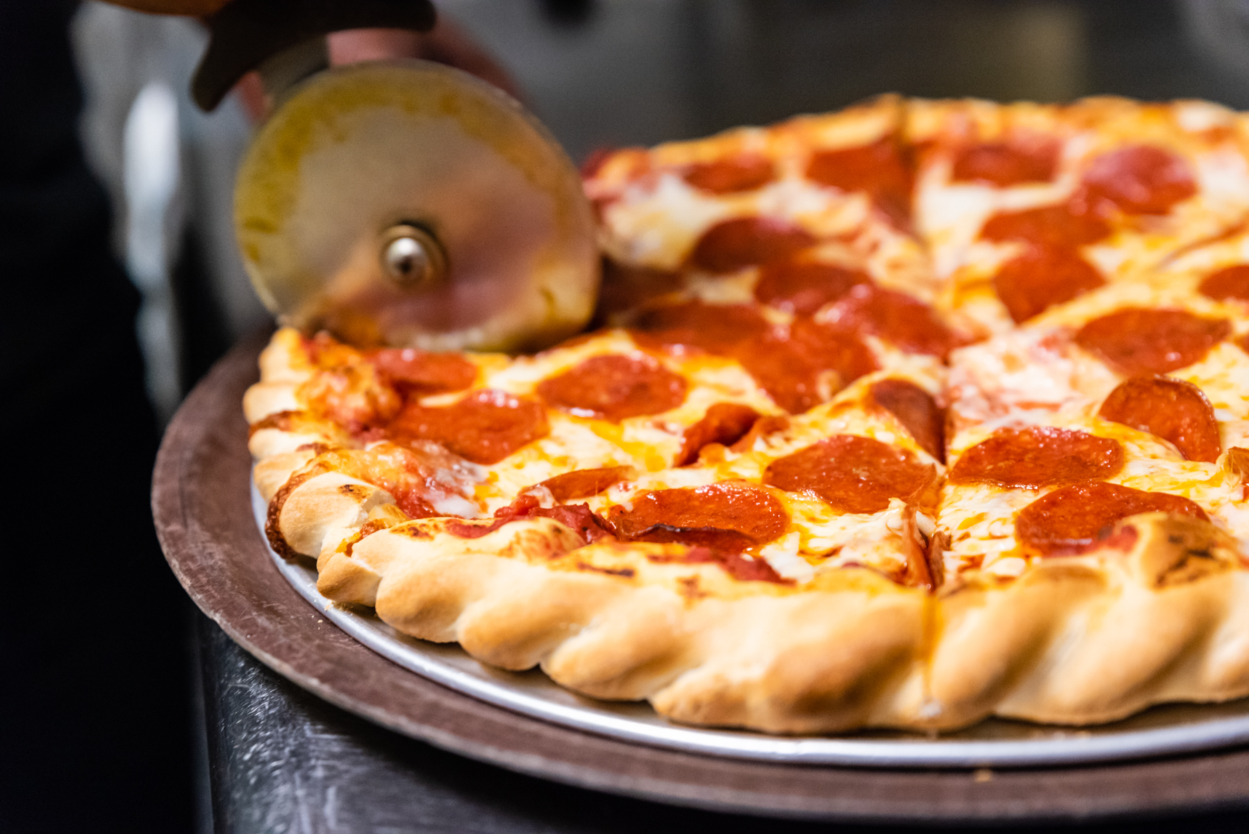 Pizza cutter slicing a pepperoni pizza on a metal pan.