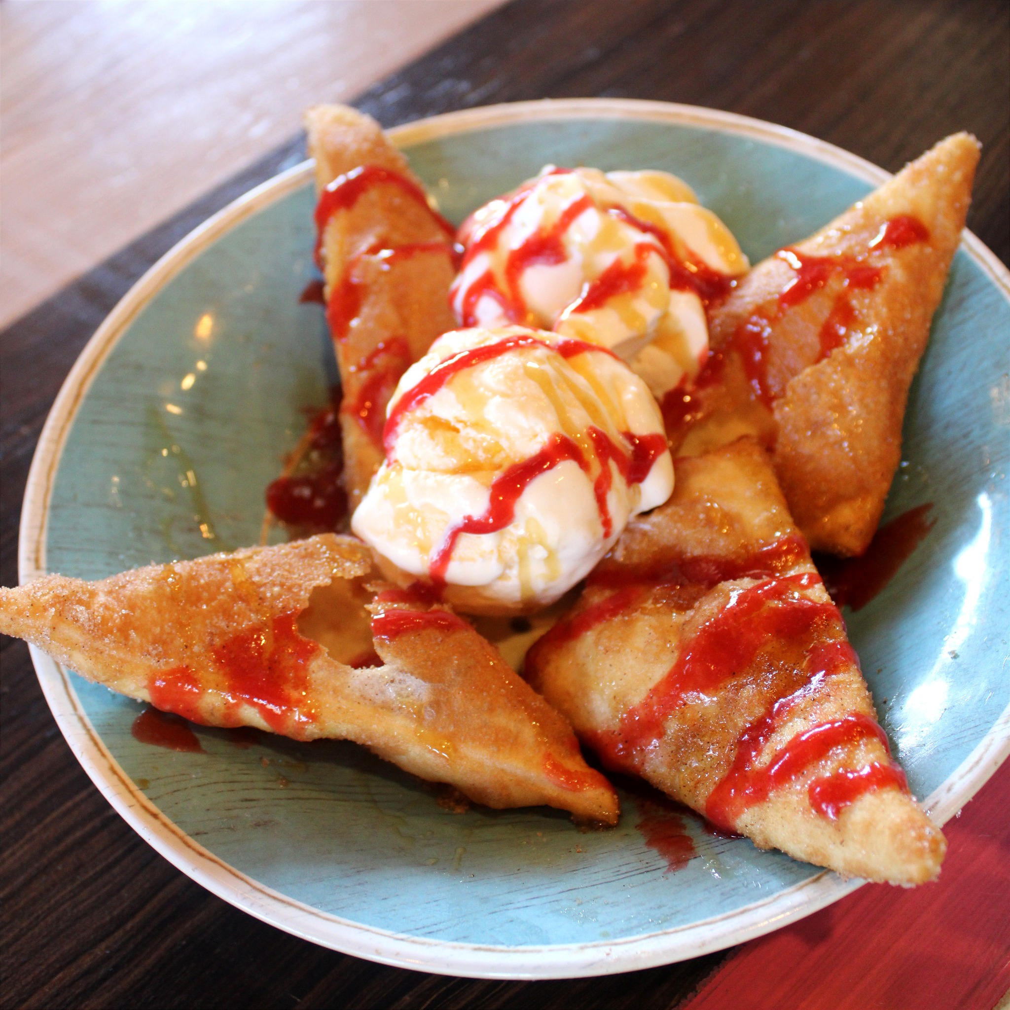 Fried pastries with vanilla ice cream, red and golden drizzles.