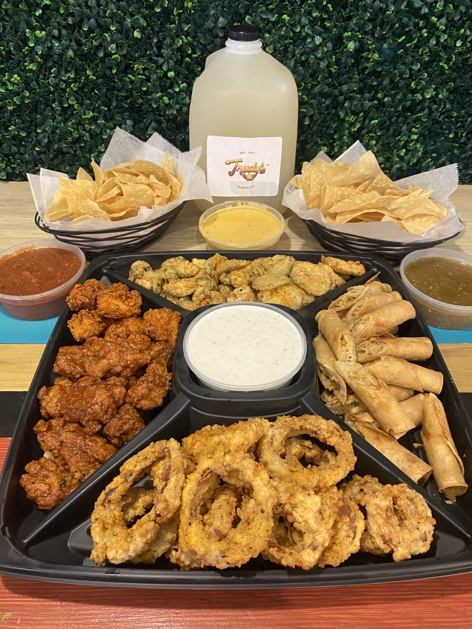 A variety platter of fried foods, chips, multiple dips, and a beverage.