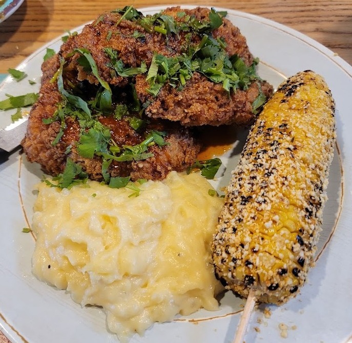 Fried chicken with cilantro, mashed potatoes, and roasted corn on a stick.