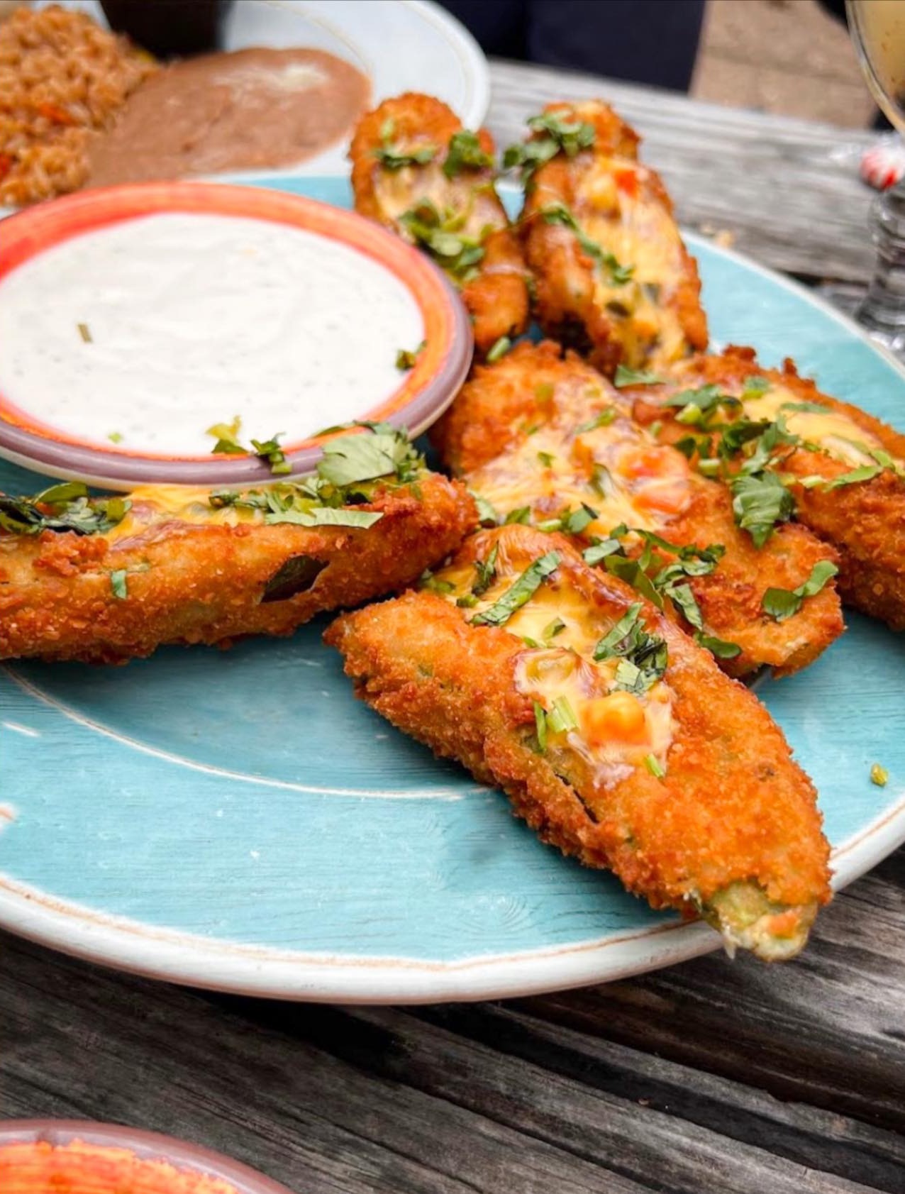Breaded fried food with melted cheese, herbs, and white dipping sauce.