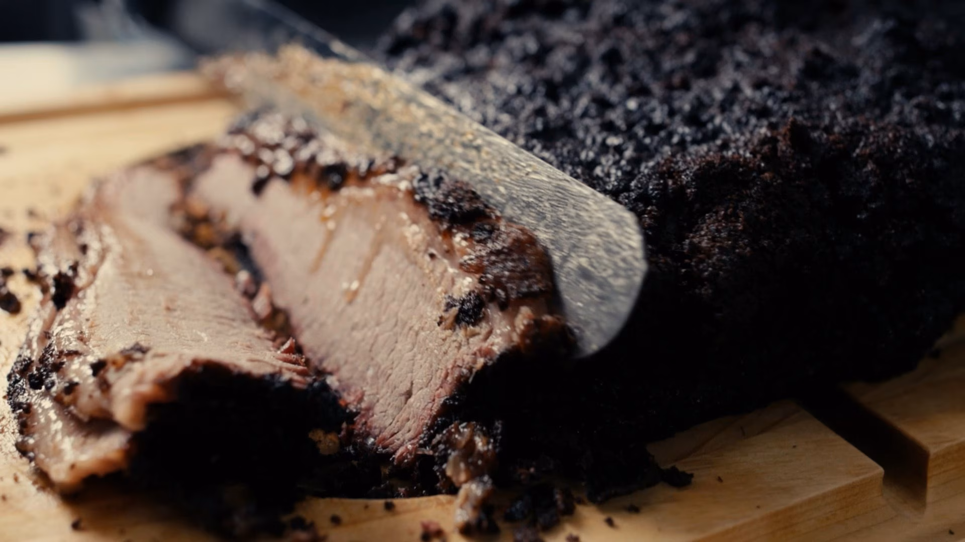 Knife slicing a dark-crusted brisket, revealing pink meat.