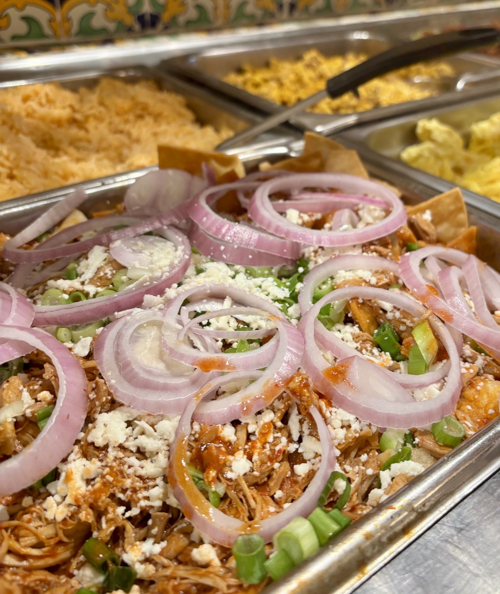 Buffet food topped with red onions, crumbled cheese, and green onions.