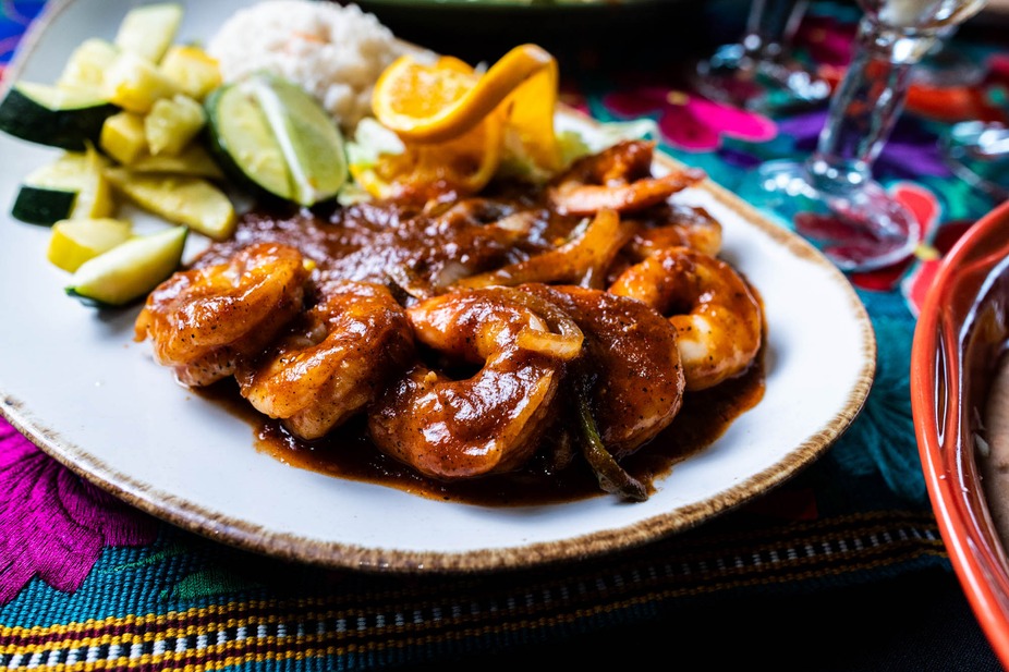 Dish of shrimp in sauce with rice, zucchini, and citrus garnishes.