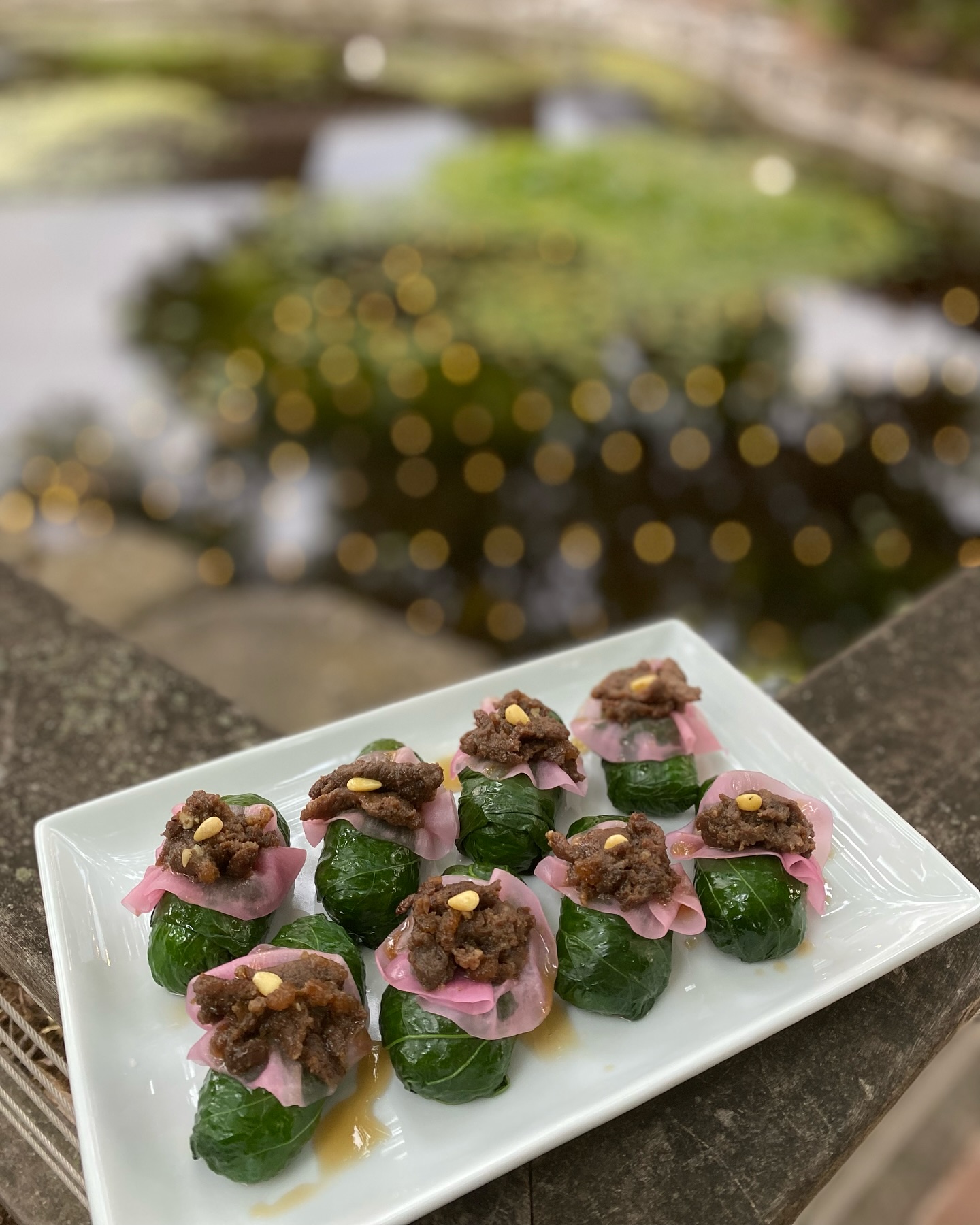 Green leaf wraps topped with meat, pink layer, and pine nuts.