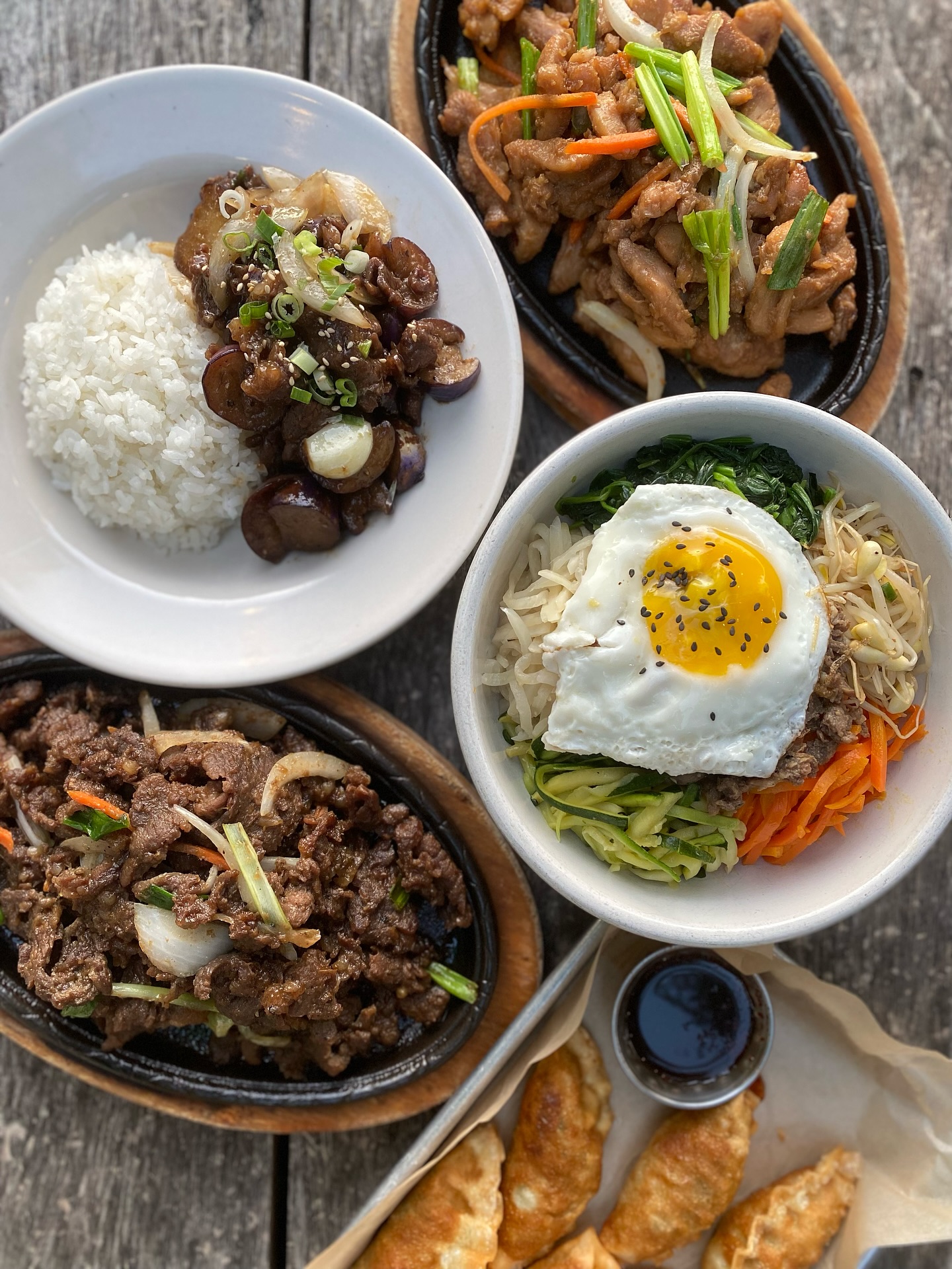 Multiple Korean dishes, including bulgogi, bibimbap, and dumplings, on a table.