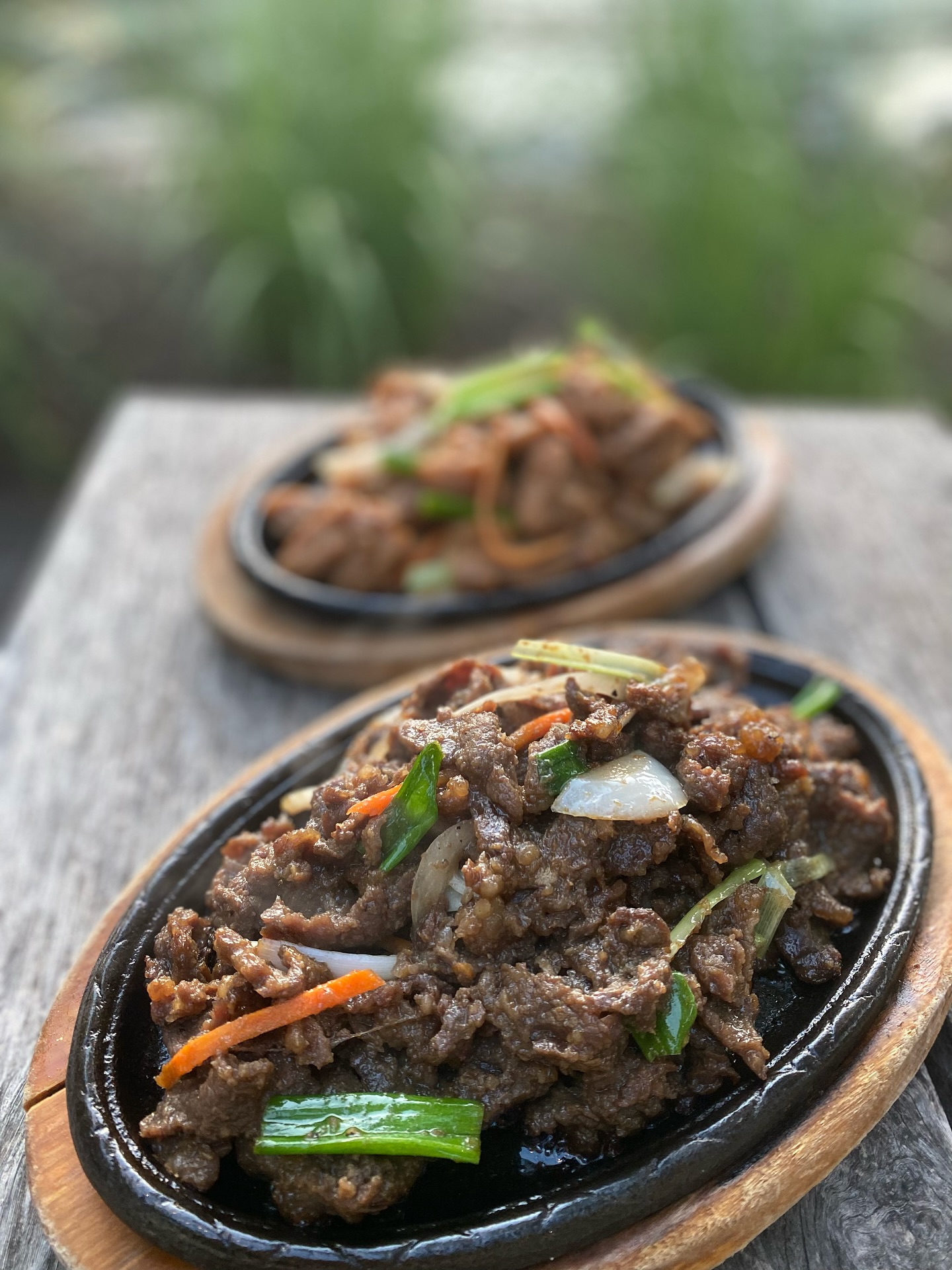 Two cast iron plates of beef with onions, carrots, green onions.