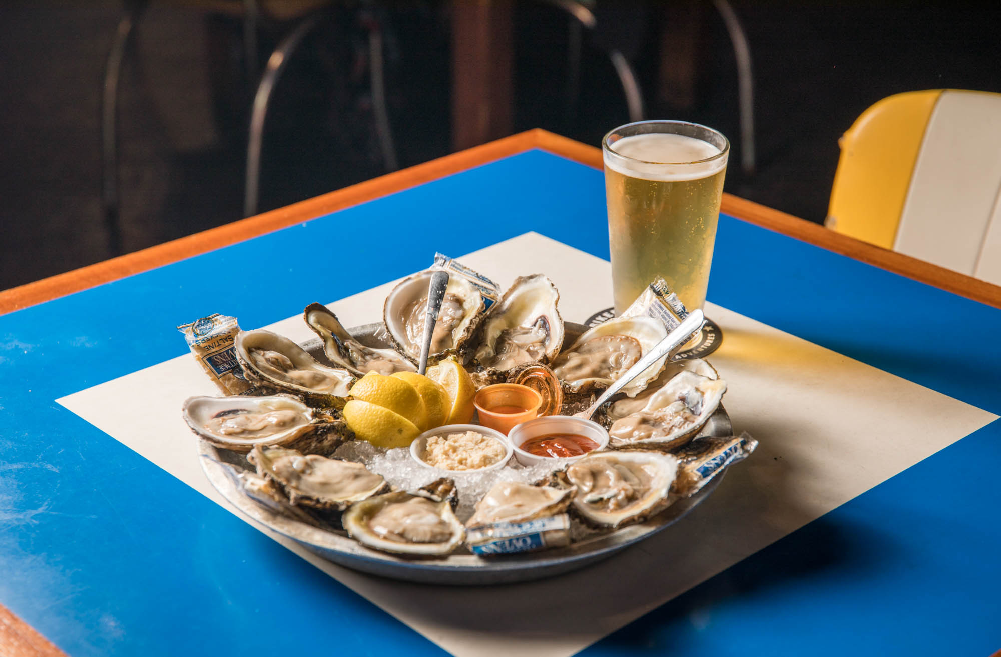 Raw oysters on ice with lemon, sauces, and a glass of beer.