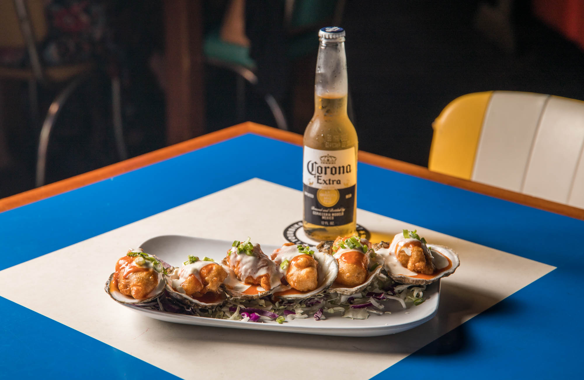 Oysters on half shells with fried toppings, sauces, and a Corona.