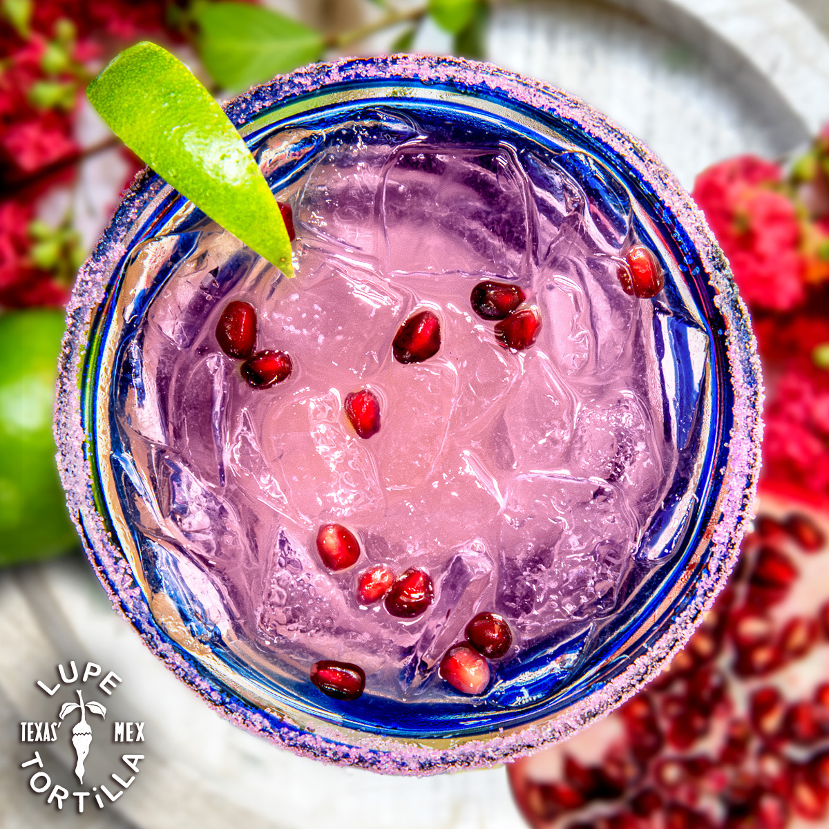 Pink drink with ice, pomegranate seeds, lime, and sugared rim.
