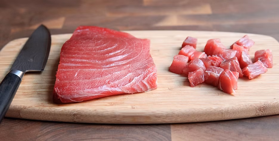 Raw tuna steak and diced pieces on a wooden cutting board.