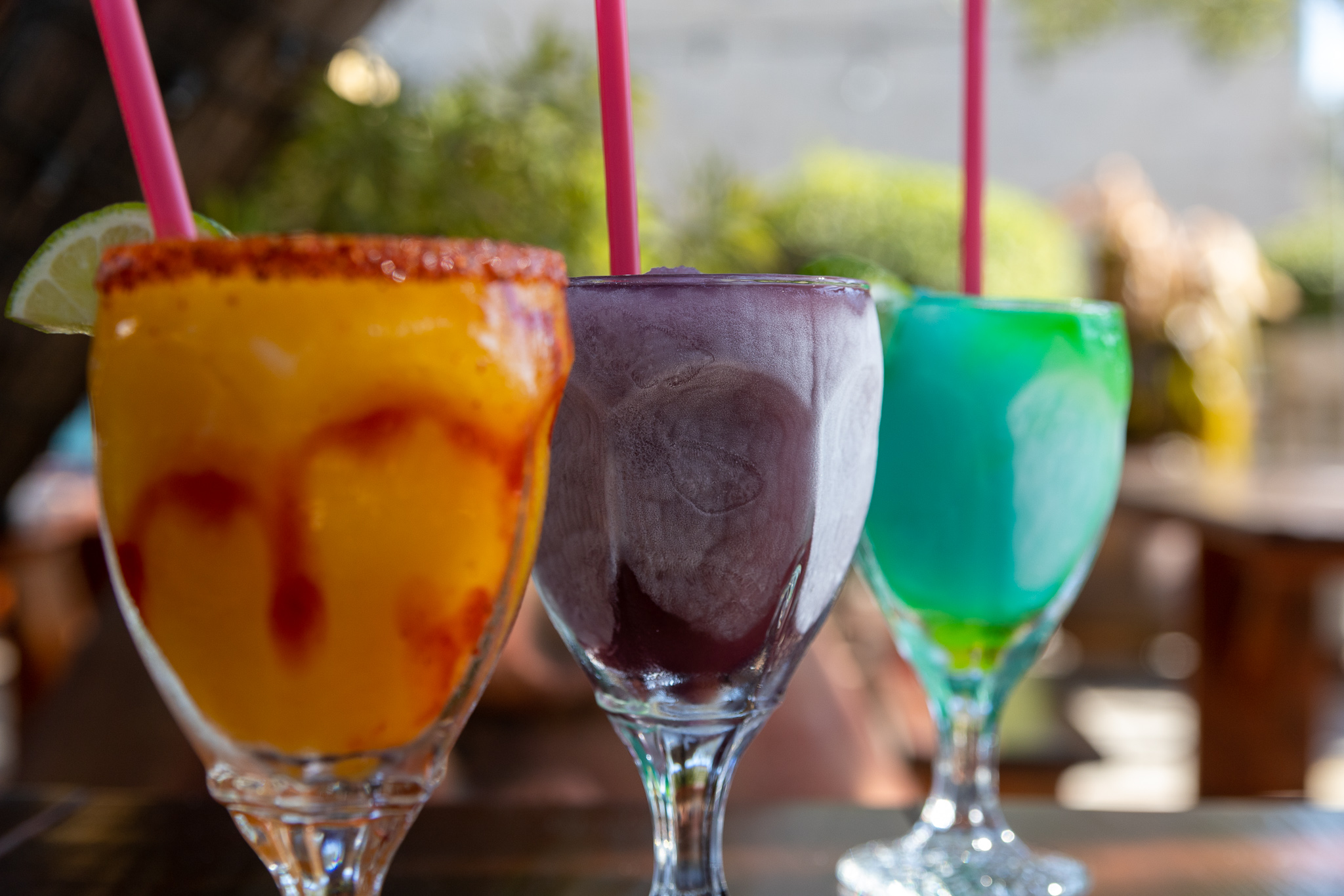 Three frozen drinks: orange, purple, and teal, with straws.