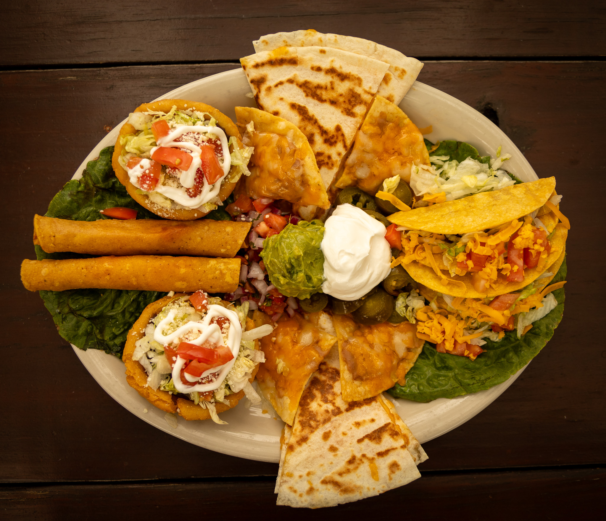 Plate of assorted Mexican food: tacos, quesadillas, taquitos, and sopes.