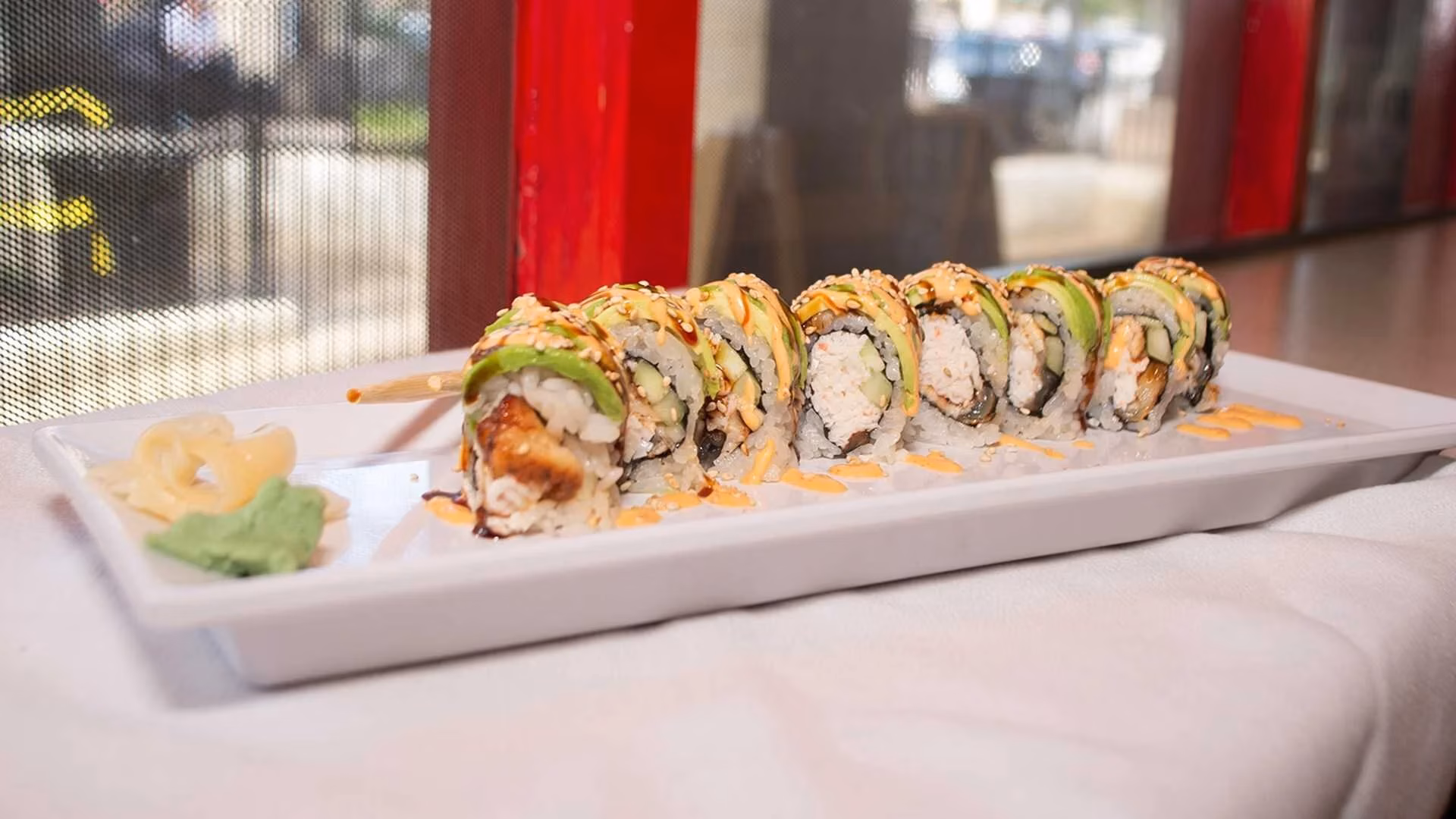 Eight sushi rolls with avocado and eel sauce on a white plate.
