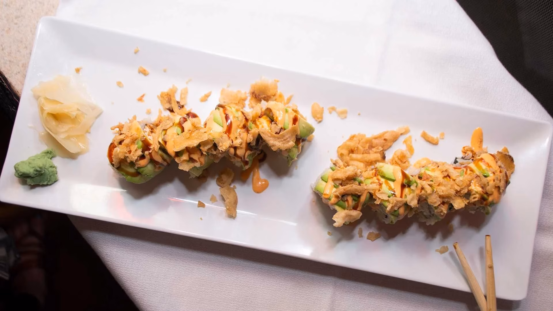 Sushi rolls topped with avocado, sauces, crispy topping, ginger, and wasabi.