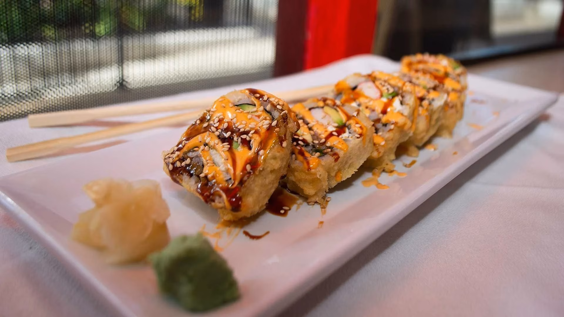 Plate of sushi rolls with sauces, sesame, pickled ginger, wasabi, chopsticks.