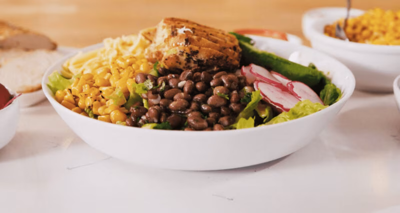 Chicken bowl with black beans, corn, radishes, and lettuce.