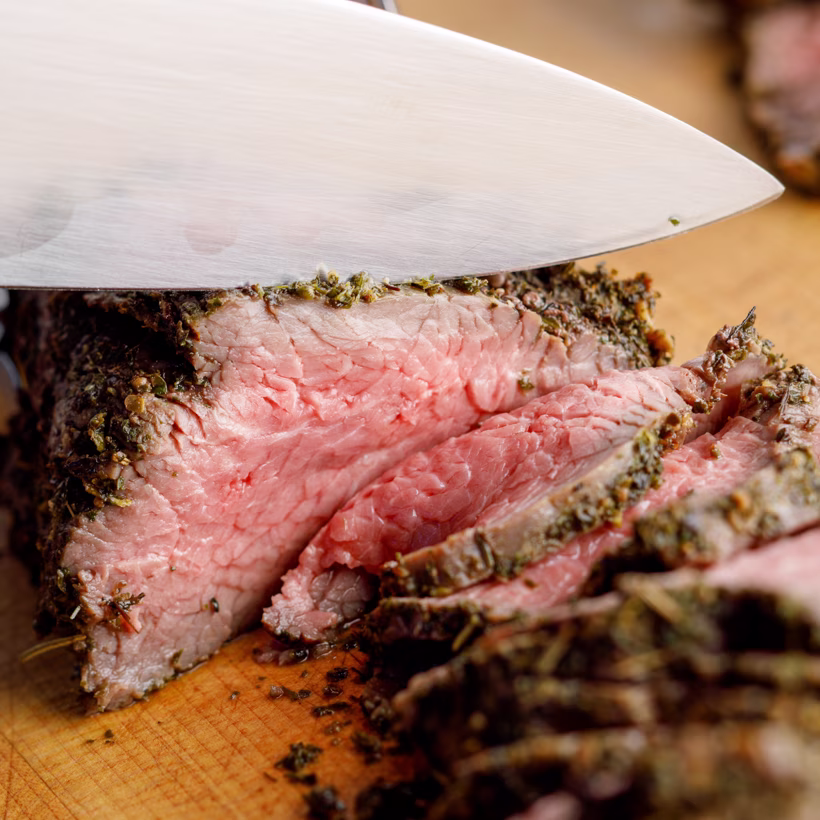 Slicing a seasoned, medium-rare roast beef on a cutting board.