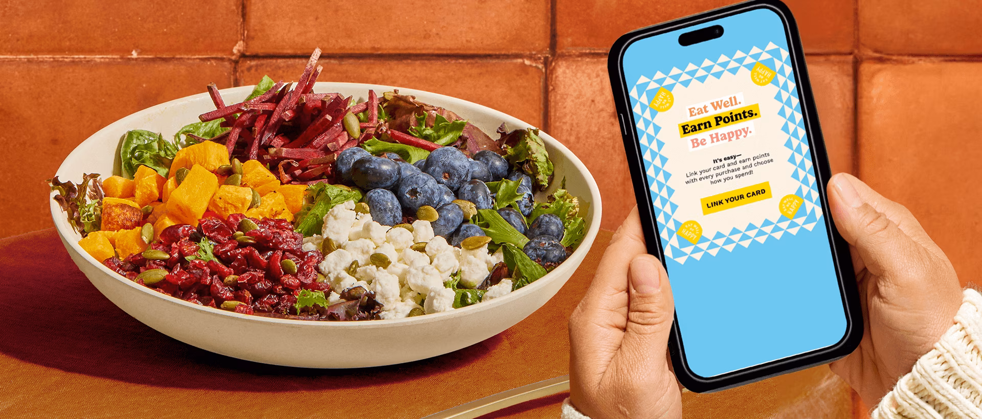 A colorful salad in a bowl next to a hand holding a phone.