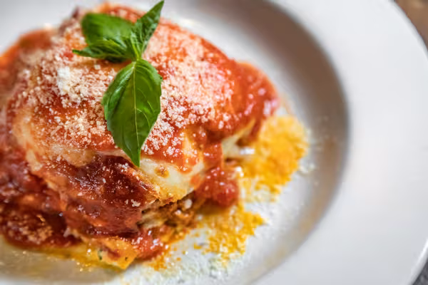 Layered pasta with red sauce, grated cheese, and basil.