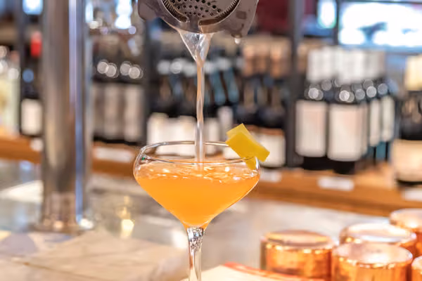 Cocktail being poured from a strainer into a garnished glass.