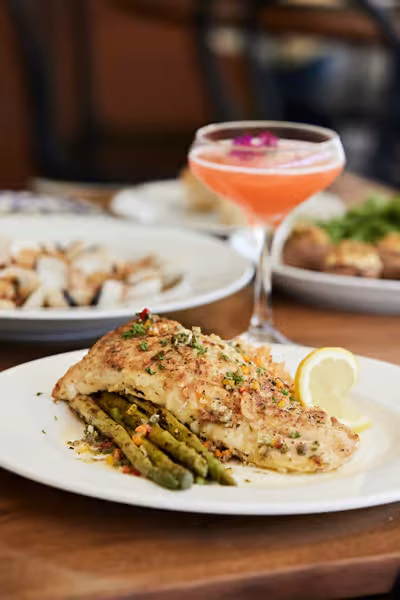 Fish fillet with asparagus and lemon, and a pink cocktail.