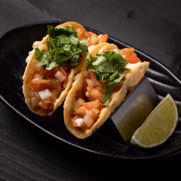 Two crispy tacos with pico de gallo, cilantro, and a lime wedge.
