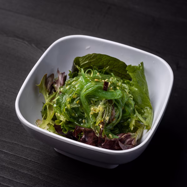 Green wakame seaweed salad with mixed greens in a white bowl.
