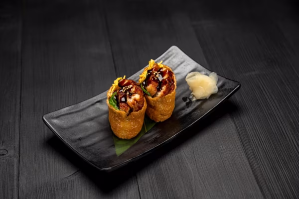 Two Inari sushi with dark filling, sauce, sesame, and ginger.