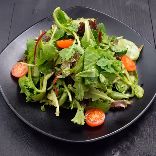 Mixed greens salad with halved cherry tomatoes on a black plate.
