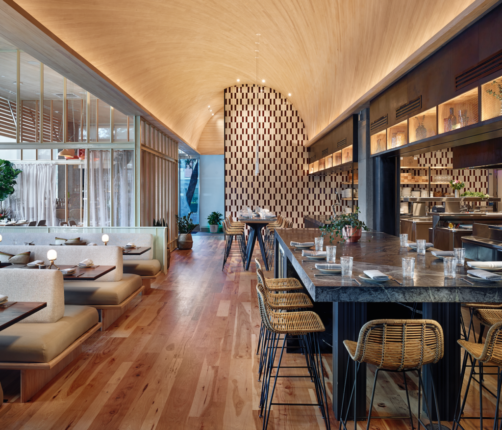 Restaurant interior with curved wooden ceiling, booths, and a long bar.