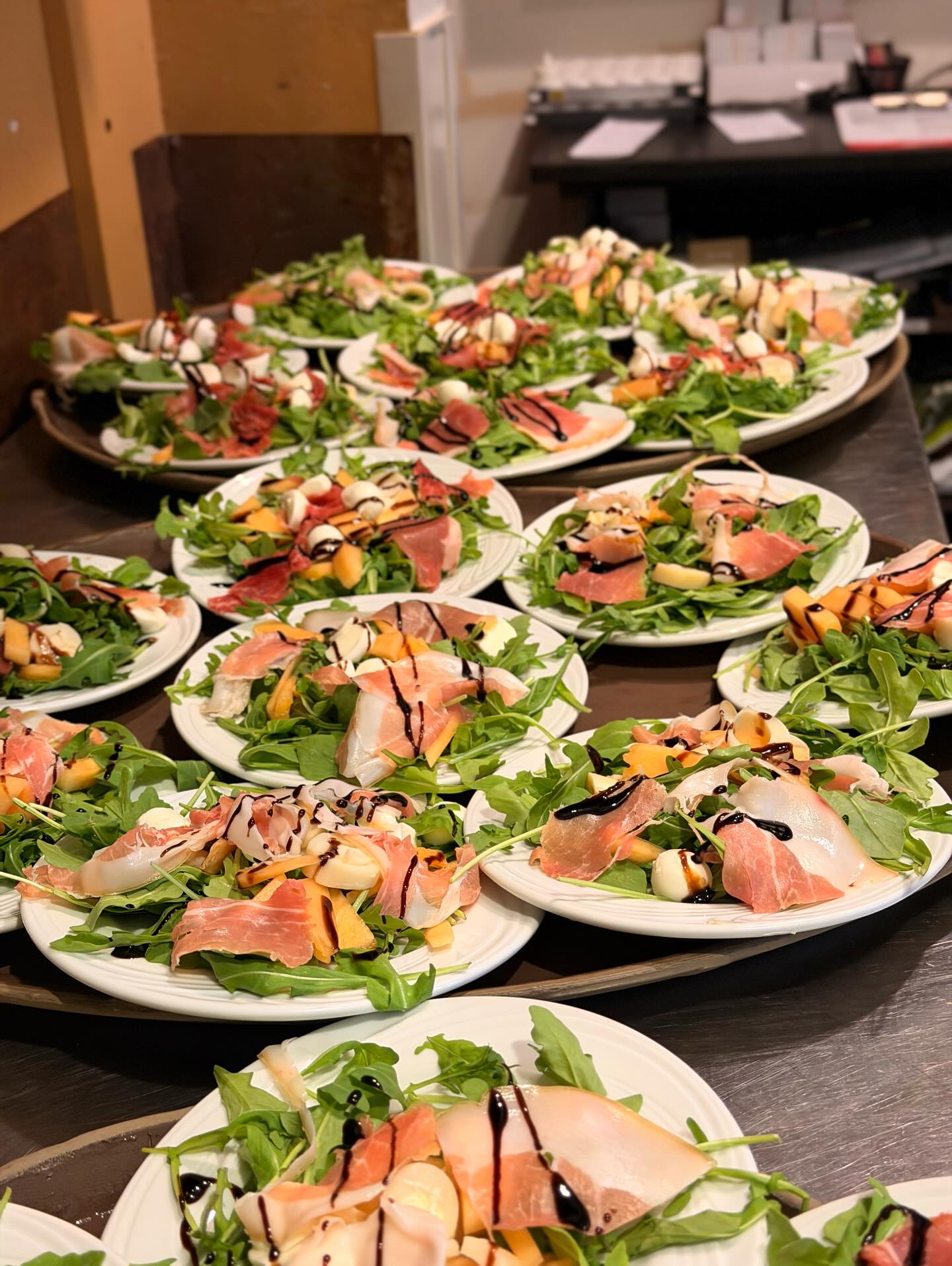 Numerous salads with prosciutto, melon, mozzarella, arugula, and balsamic glaze.