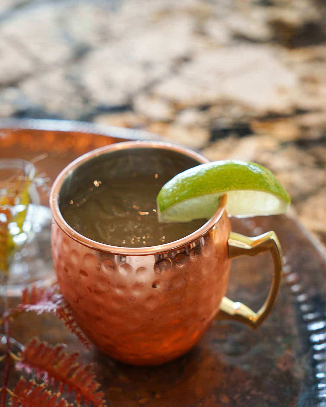 Hammered copper mug with a drink, ice, and lime garnish.