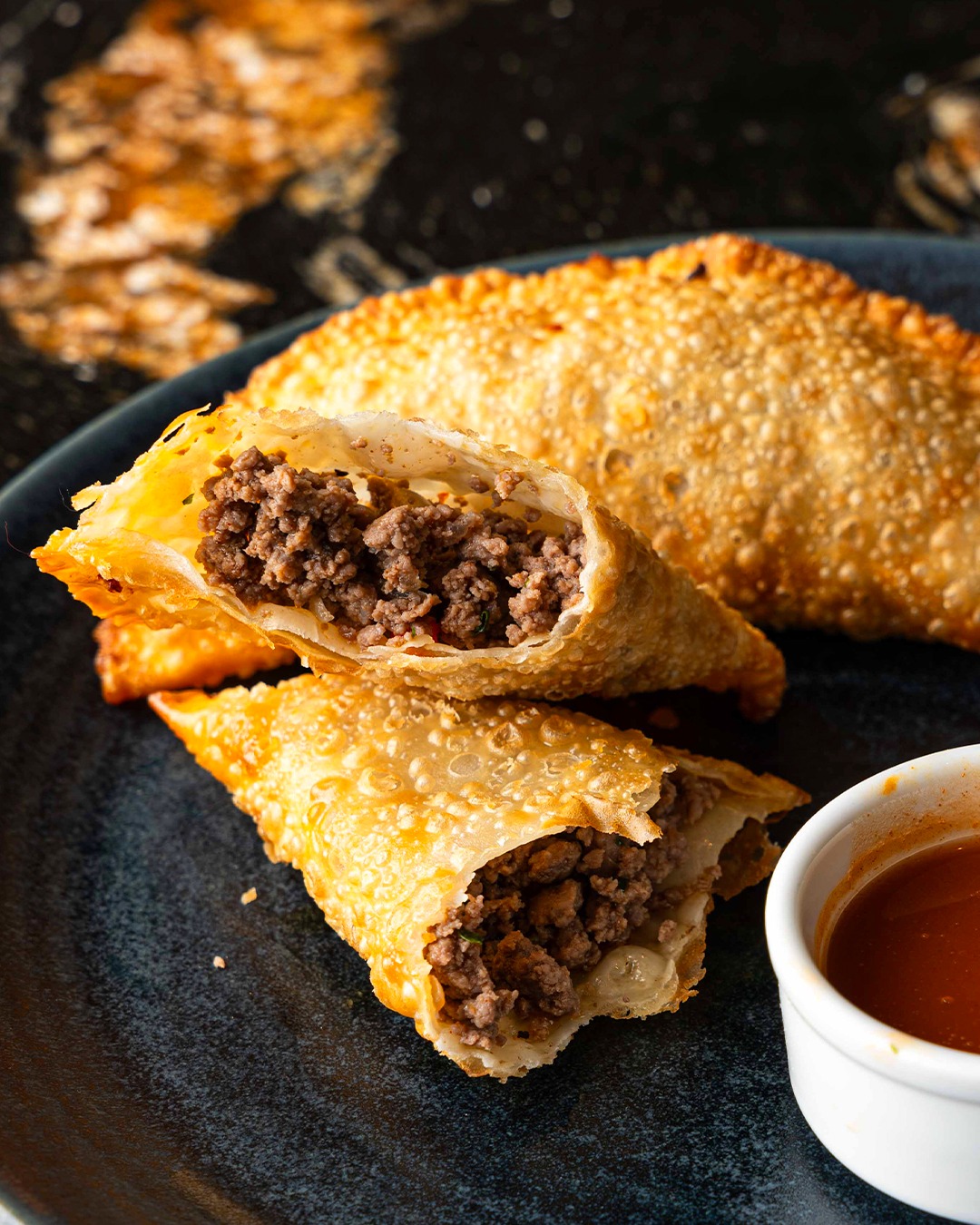 Golden fried pastries filled with ground meat, served with sauce.