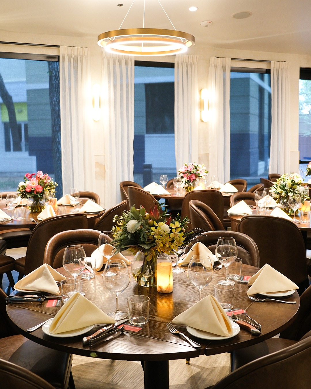 Modern dining room with round tables, place settings, and floral centerpieces.