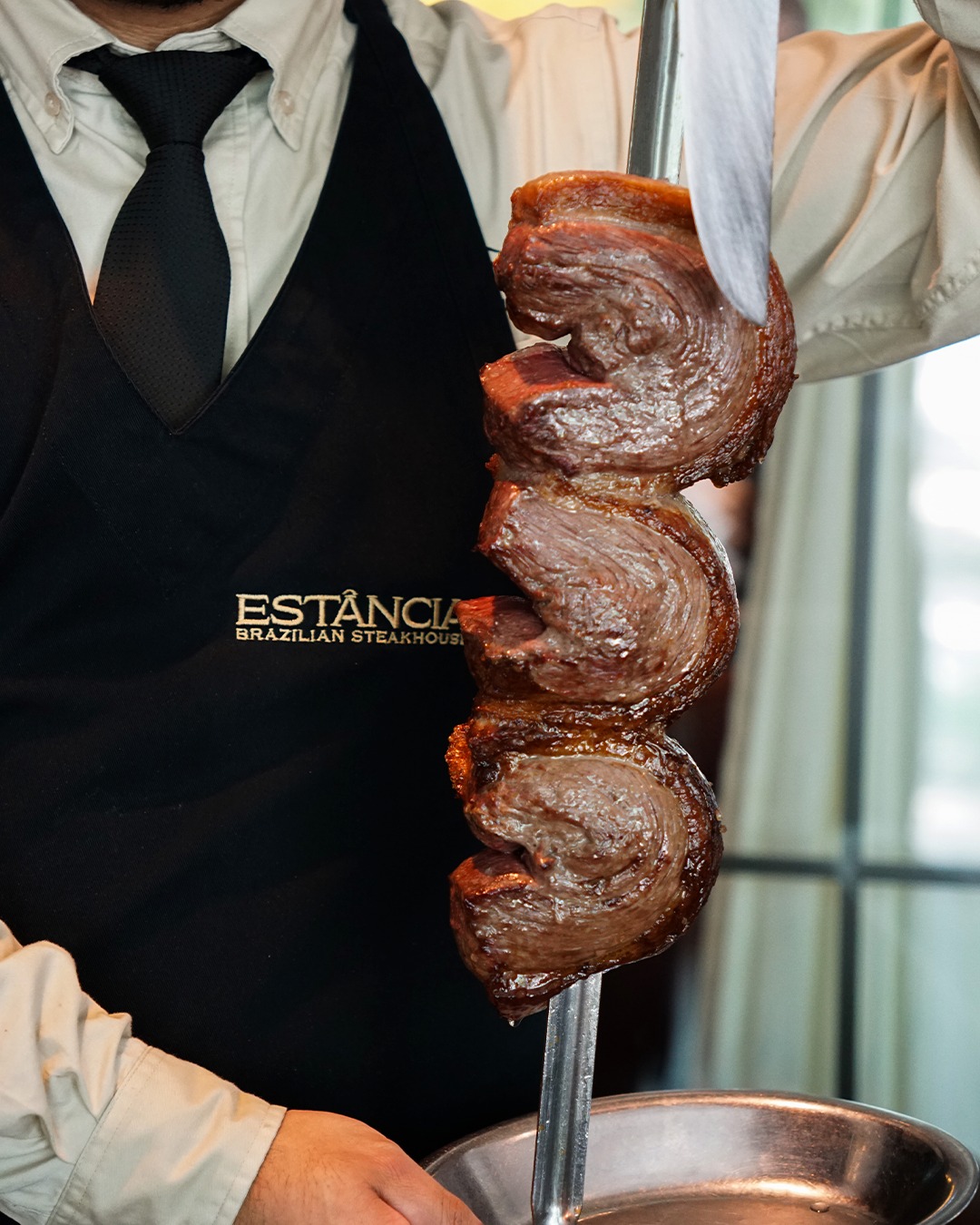 Server carving roasted meat from a skewer at a Brazilian steakhouse.