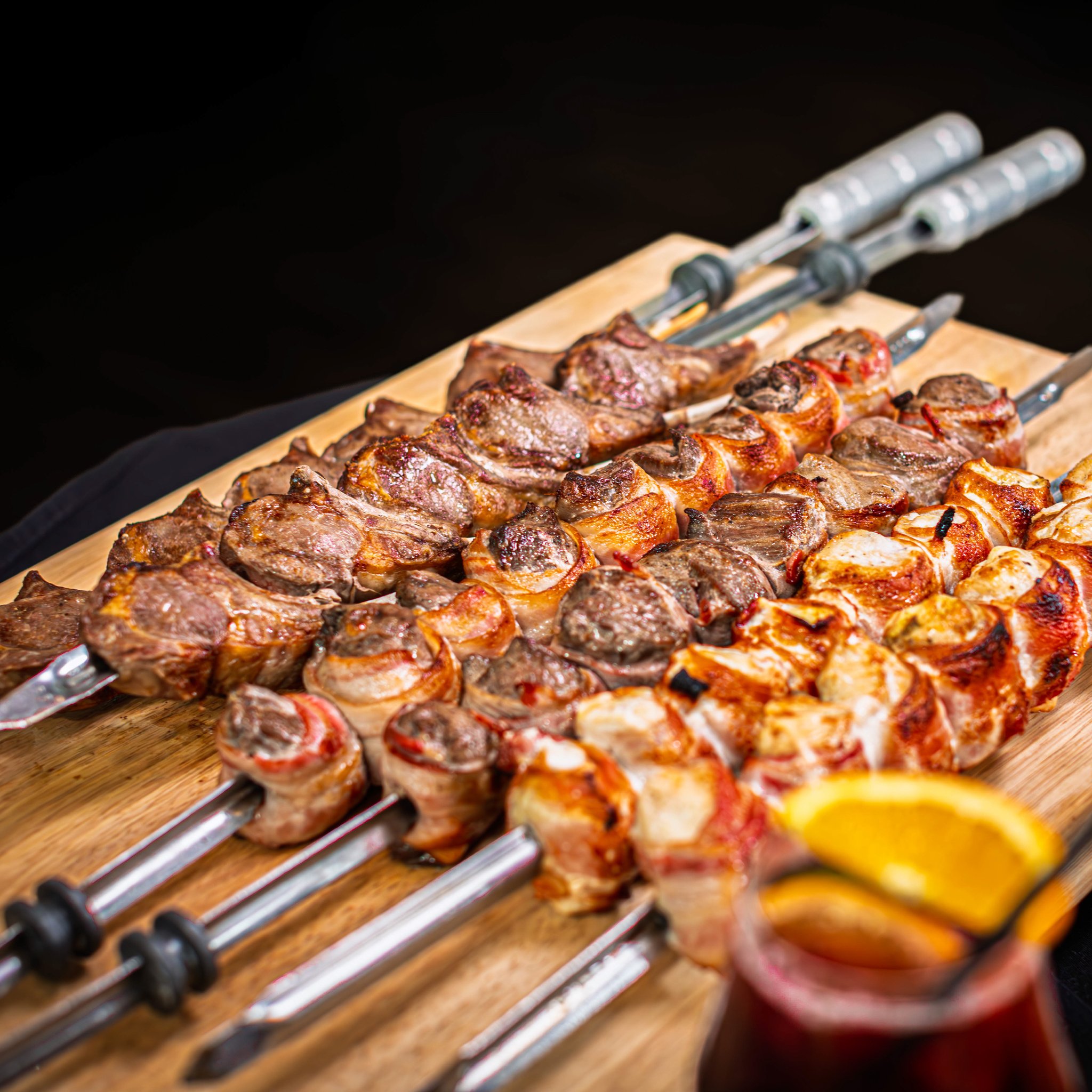 Cooked meat skewers, some bacon-wrapped, arranged on a wooden board.